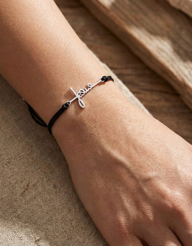 Mulher a usar no pulso uma pulseira preta de fio com o nome 'Jesus' em metal prateado.